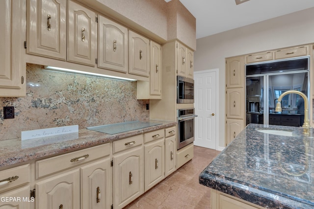kitchen with cream cabinets, a sink, stone countertops, backsplash, and black appliances