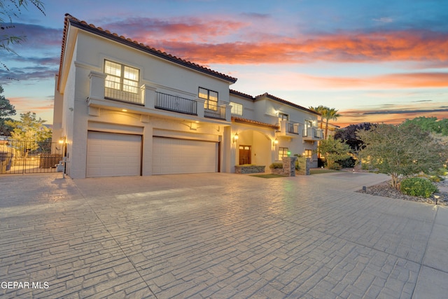 mediterranean / spanish-style home featuring an attached garage, stucco siding, a balcony, and fence