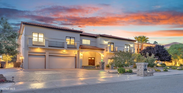 mediterranean / spanish-style house with a tile roof, an attached garage, a balcony, and stucco siding