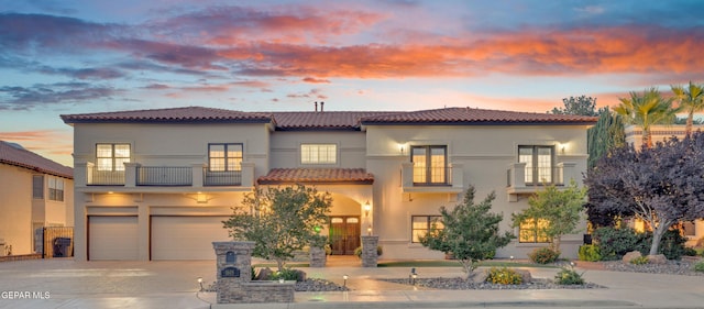 mediterranean / spanish-style house featuring a garage, a balcony, stucco siding, a tiled roof, and concrete driveway