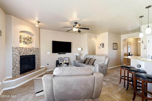 tiled living area with arched walkways, a tile fireplace, baseboards, and ceiling fan