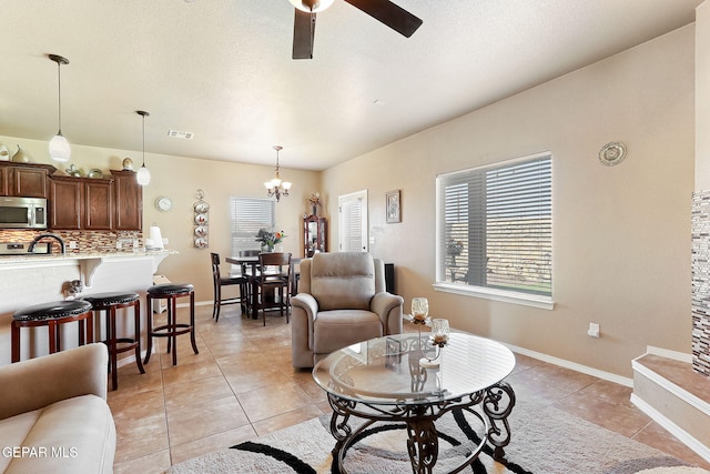 living room featuring ceiling fan with notable chandelier, baseboards, visible vents, and light tile patterned floors