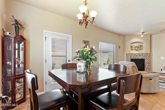 dining room with an inviting chandelier, a stone fireplace, and light tile patterned floors