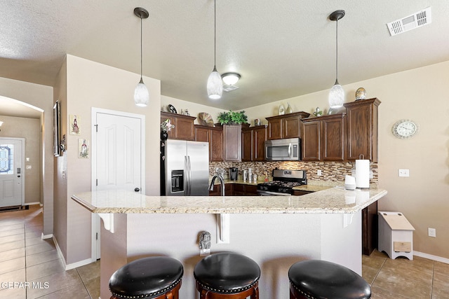 kitchen with visible vents, light tile patterned floors, a kitchen bar, tasteful backsplash, and appliances with stainless steel finishes