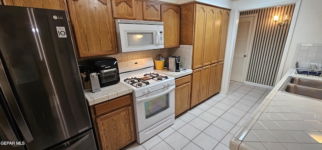 2704 Gaston Dr, El Paso, TX 79935 - kitchen featuring a sink, tile counters, light tile patterned floors, tasteful backsplash, and white appliances