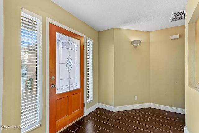 entrance foyer with baseboards, wood tiled floor, a textured ceiling, and visible vents