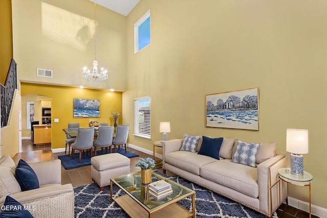 tiled living room featuring a notable chandelier, arched walkways, baseboards, a towering ceiling, and visible vents