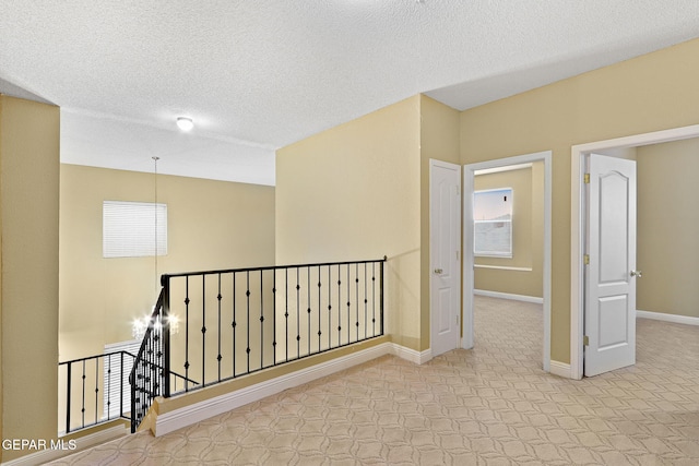 corridor with baseboards, a textured ceiling, tile patterned floors, and an upstairs landing