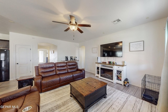 living area with ceiling fan, arched walkways, light wood-style flooring, baseboards, and visible vents