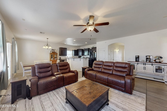 living area featuring recessed lighting, light wood finished floors, visible vents, arched walkways, and ceiling fan with notable chandelier