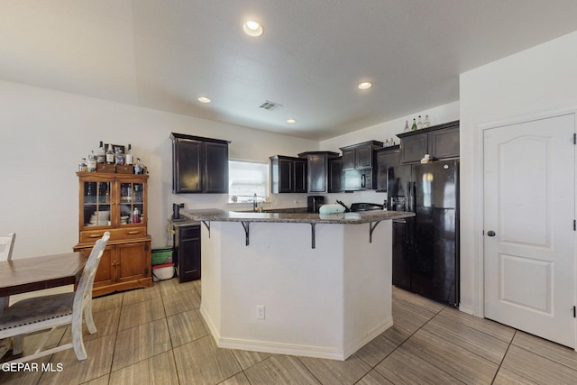 kitchen featuring visible vents, a center island, dark stone counters, black appliances, and a breakfast bar area