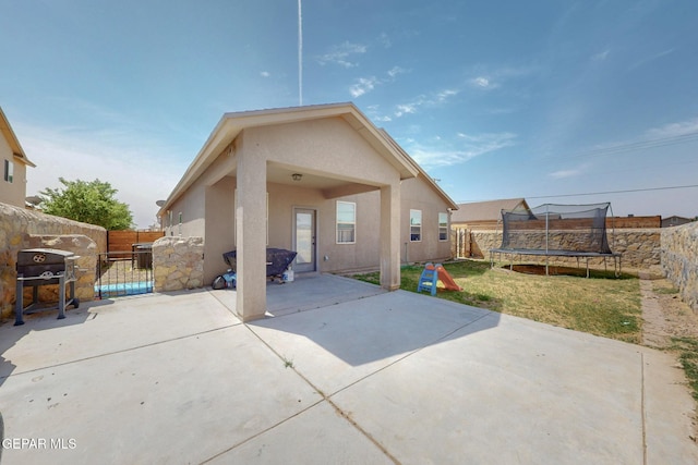 back of house with a trampoline, a patio area, a fenced backyard, and stucco siding