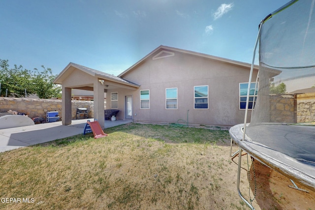 back of house featuring a yard, a trampoline, a patio area, and stucco siding