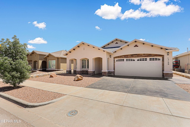 mediterranean / spanish-style house with an attached garage, stucco siding, driveway, and stone siding