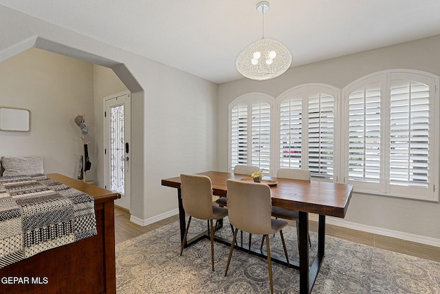 dining area with baseboards, arched walkways, light wood finished floors, and an inviting chandelier