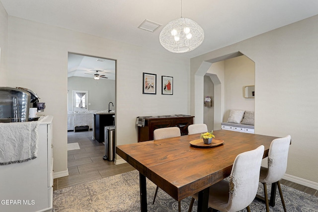 dining room featuring arched walkways, ceiling fan with notable chandelier, baseboards, light wood-type flooring, and visible vents