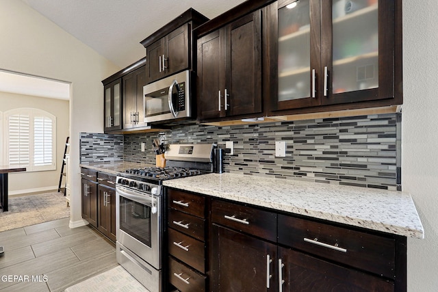 kitchen featuring lofted ceiling, dark brown cabinetry, tasteful backsplash, light stone counters, and stainless steel appliances
