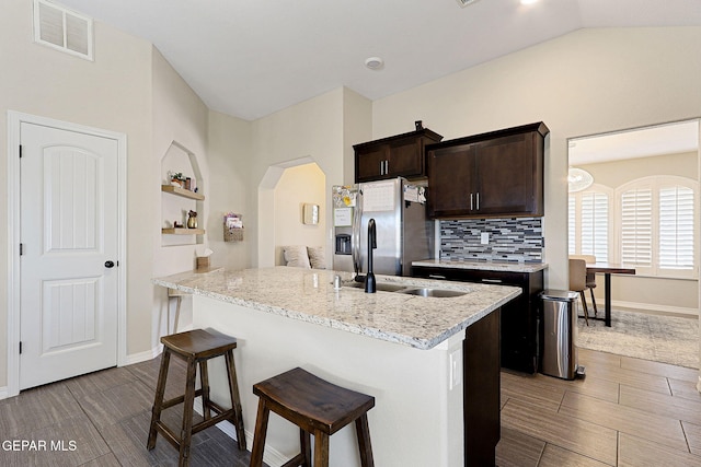 kitchen featuring a breakfast bar area, stainless steel refrigerator with ice dispenser, visible vents, dark brown cabinets, and baseboards