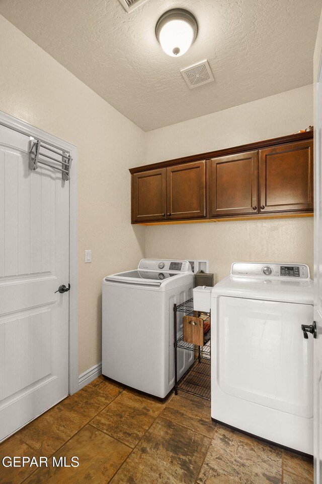 laundry area with cabinet space, a textured ceiling, visible vents, and washer and clothes dryer