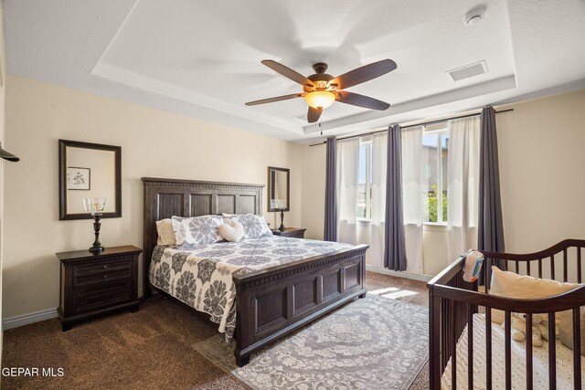 bedroom with a tray ceiling, dark colored carpet, visible vents, and baseboards