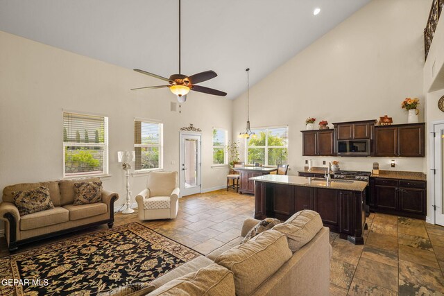 living area featuring stone tile flooring, baseboards, a ceiling fan, and high vaulted ceiling
