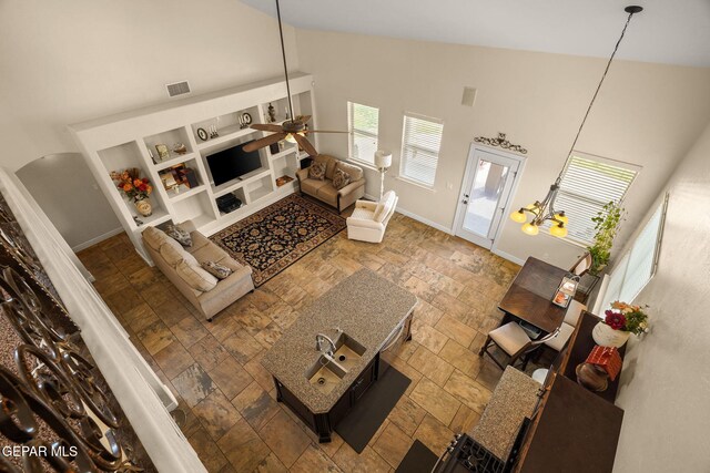 living area with high vaulted ceiling, ceiling fan, stone tile flooring, baseboards, and visible vents