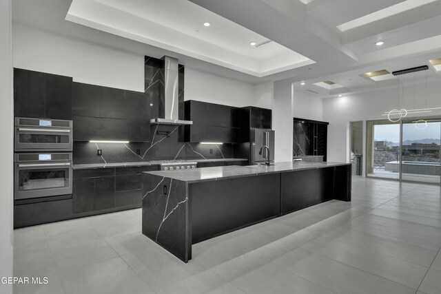 kitchen featuring dark cabinetry, modern cabinets, a large island with sink, and wall chimney exhaust hood