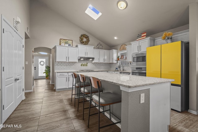 kitchen with appliances with stainless steel finishes, under cabinet range hood, tasteful backsplash, a center island, and white cabinetry