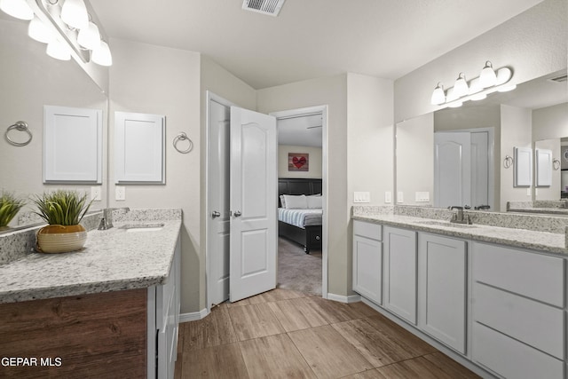 ensuite bathroom with wood finish floors, two vanities, and baseboards