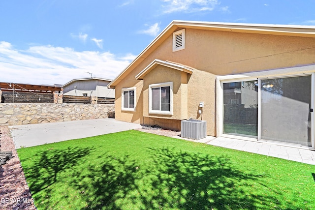 rear view of property featuring central AC, fence, a yard, a patio, and stucco siding
