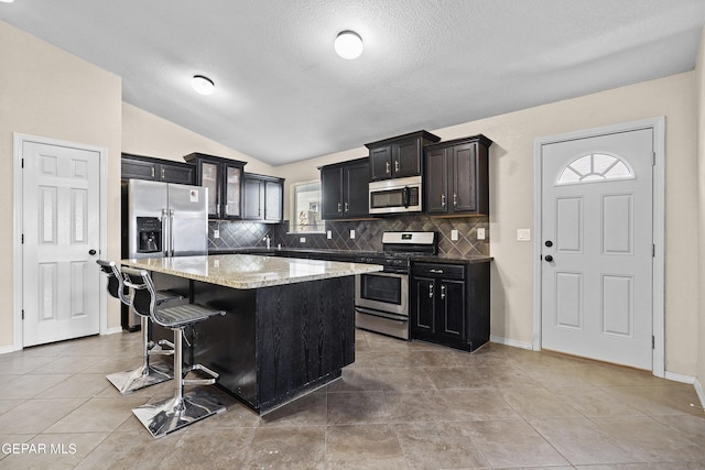 kitchen featuring a kitchen island, backsplash, a textured ceiling, appliances with stainless steel finishes, and light stone countertops