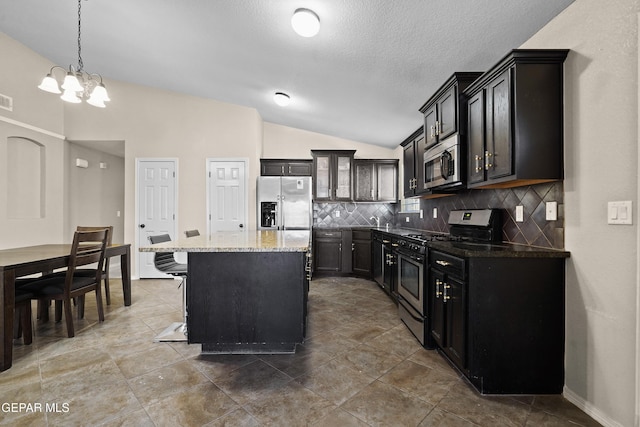 kitchen with a notable chandelier, appliances with stainless steel finishes, stone countertops, lofted ceiling, and tasteful backsplash