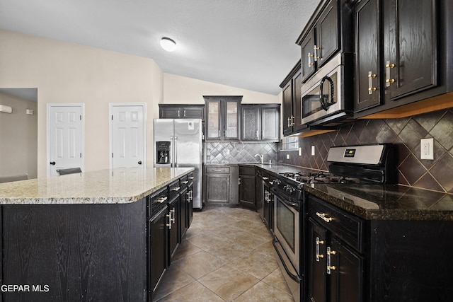 kitchen with decorative backsplash, lofted ceiling, a center island, dark cabinetry, and appliances with stainless steel finishes