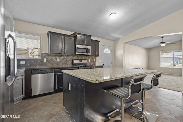 kitchen featuring appliances with stainless steel finishes, a kitchen breakfast bar, tasteful backsplash, a kitchen island, and vaulted ceiling