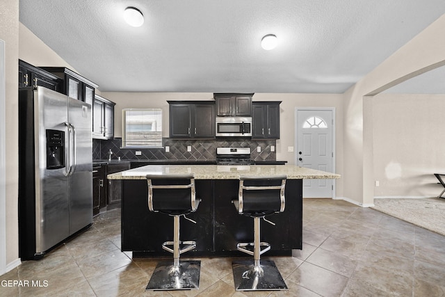 kitchen with a kitchen island, light stone countertops, a textured ceiling, backsplash, and stainless steel appliances