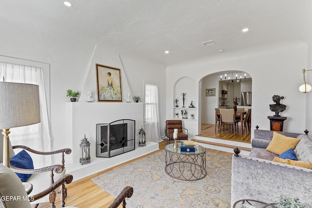 living area with an inviting chandelier, arched walkways, a fireplace with raised hearth, recessed lighting, and wood finished floors