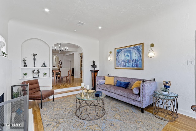 living room featuring visible vents, wood finished floors, baseboards, arched walkways, and a notable chandelier