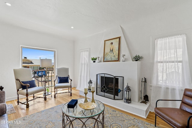 living area featuring baseboards, a fireplace with raised hearth, recessed lighting, and wood finished floors
