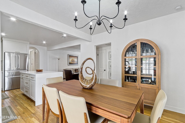 dining area featuring light wood finished floors, arched walkways, a chandelier, baseboards, and beamed ceiling