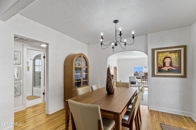dining space featuring light wood-style floors, arched walkways, a textured wall, and a chandelier