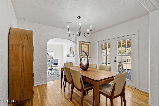 dining room featuring baseboards, arched walkways, a textured wall, and light wood-style flooring