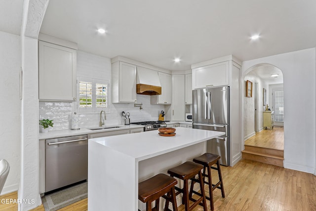 kitchen featuring light wood-style floors, arched walkways, custom range hood, a sink, and stainless steel appliances