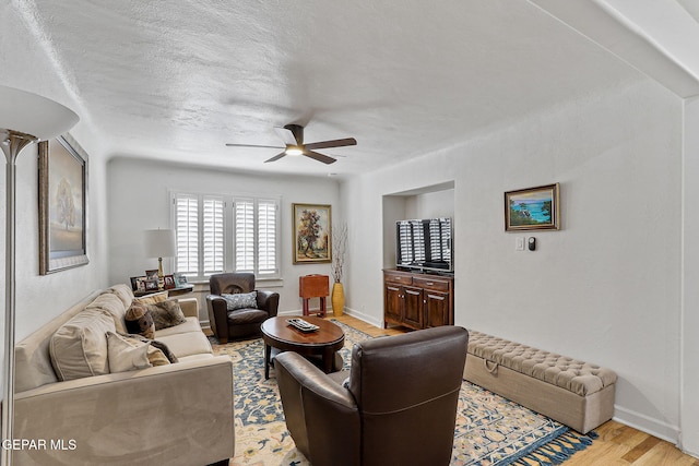 living room featuring baseboards, a ceiling fan, and light wood finished floors