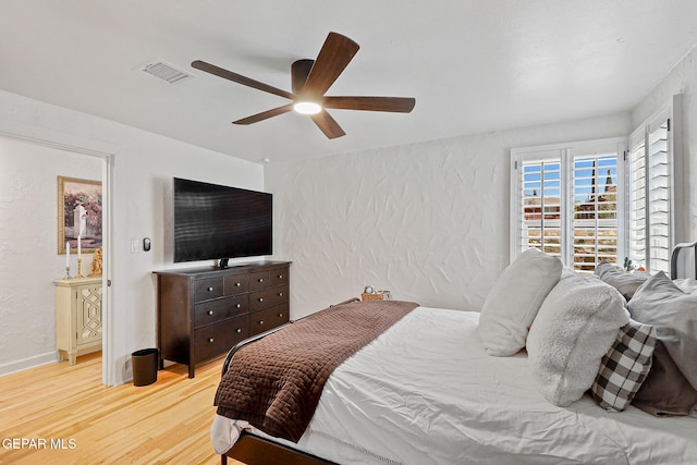 bedroom featuring a textured wall, visible vents, ceiling fan, and light wood finished floors
