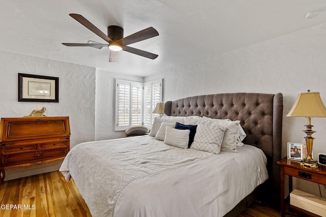bedroom with a ceiling fan, a textured wall, and wood finished floors