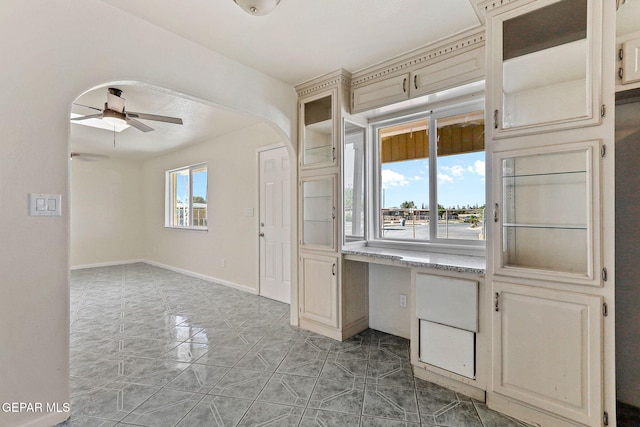 interior space with ceiling fan, baseboards, and arched walkways