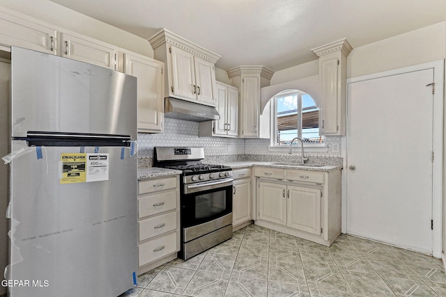 kitchen featuring a sink, appliances with stainless steel finishes, under cabinet range hood, light stone countertops, and backsplash