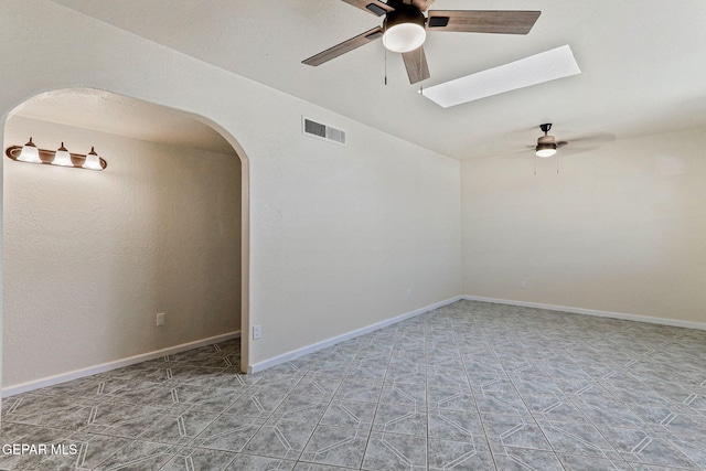 empty room with a skylight, visible vents, ceiling fan, and arched walkways