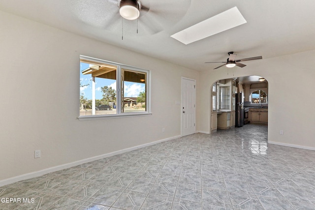 unfurnished living room featuring a skylight, ceiling fan, baseboards, and arched walkways