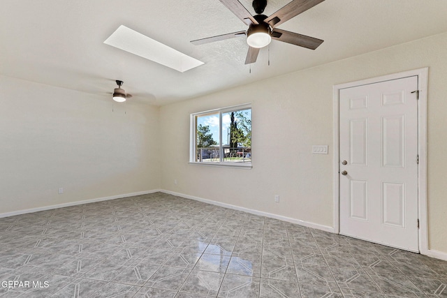 unfurnished room featuring a skylight, ceiling fan, and baseboards